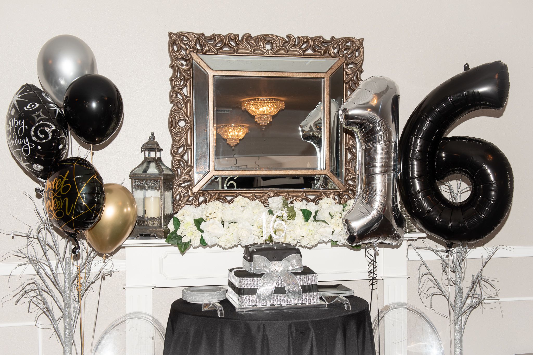 Elegant party setup featuring silver and black number 16 balloons, framed art, floral decorations and metallic balloon bouquets.