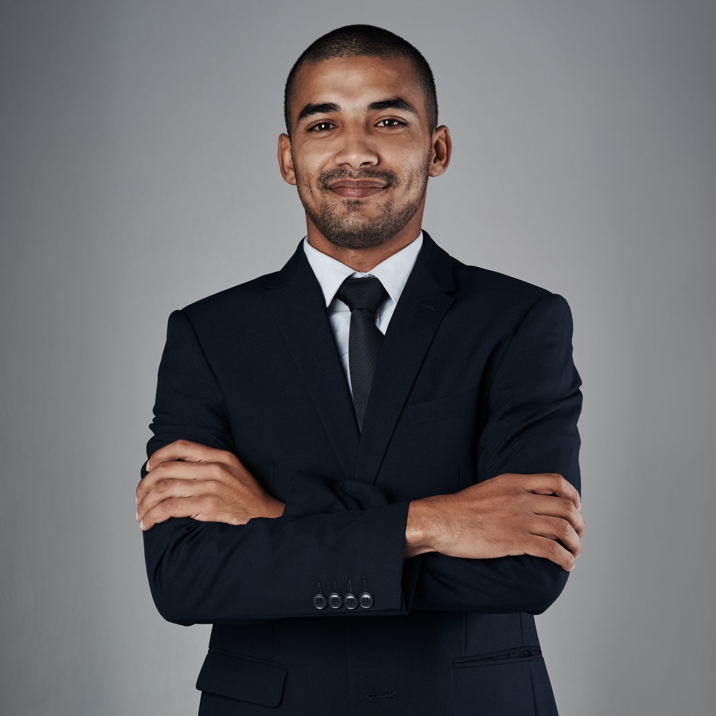 Professional portrait of a businessman in a dark suit and tie with arms crossed against a gray background.