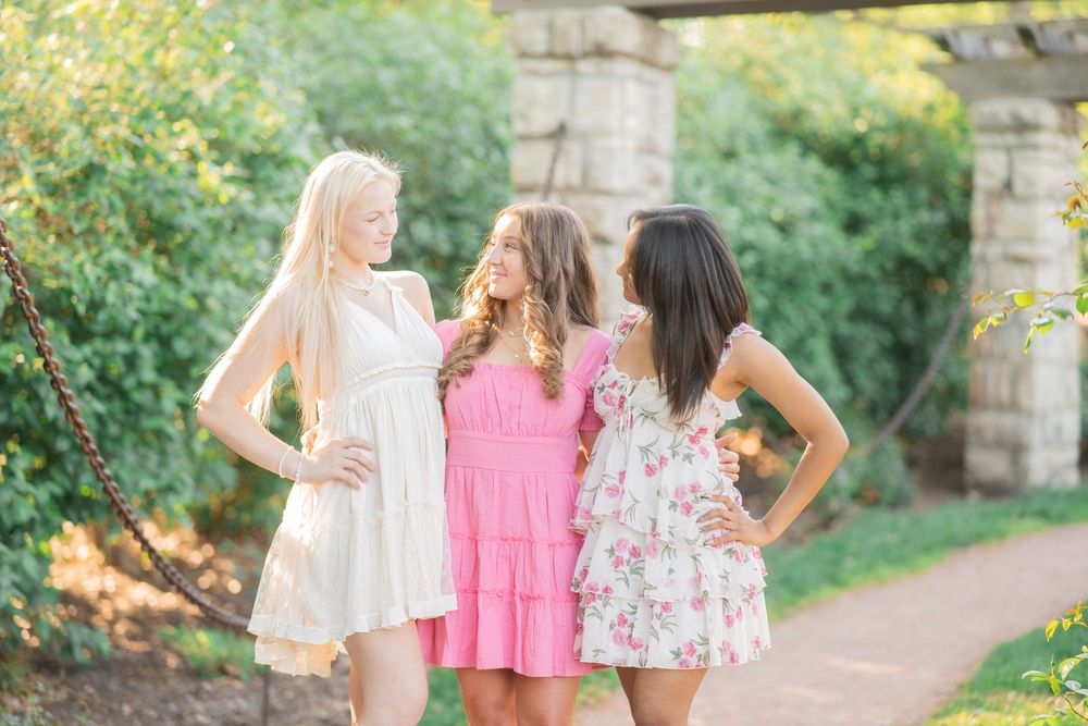 Three teen girls in colorful summer dresses chatting together on a garden path.