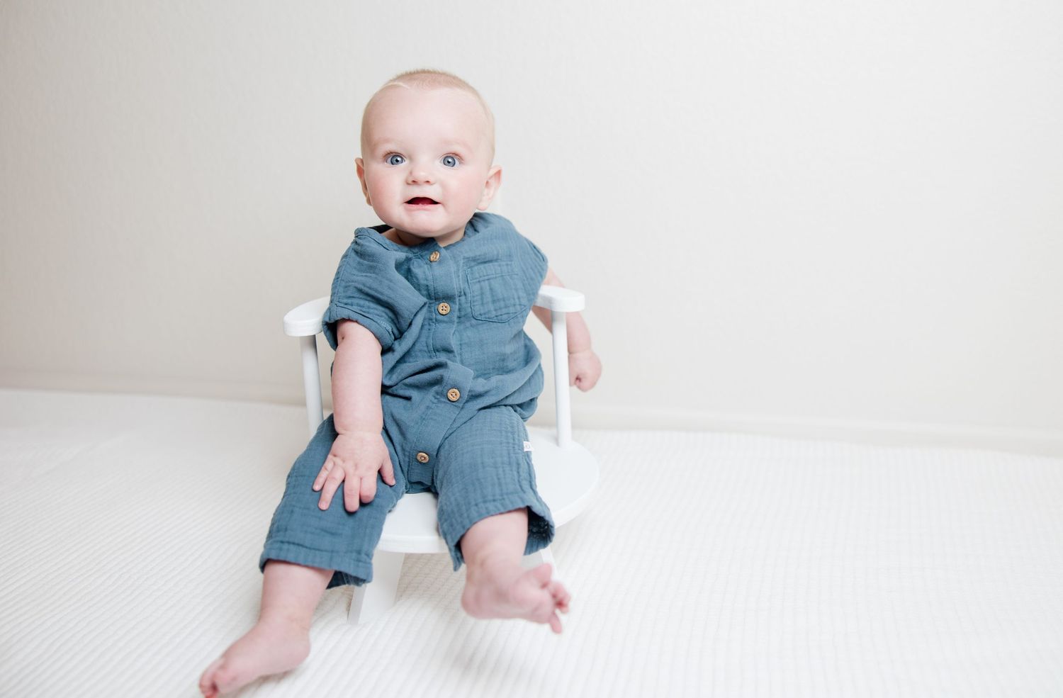 Baby wearing mint green ruffled outfit lies on cream colored carpet looking to the side.