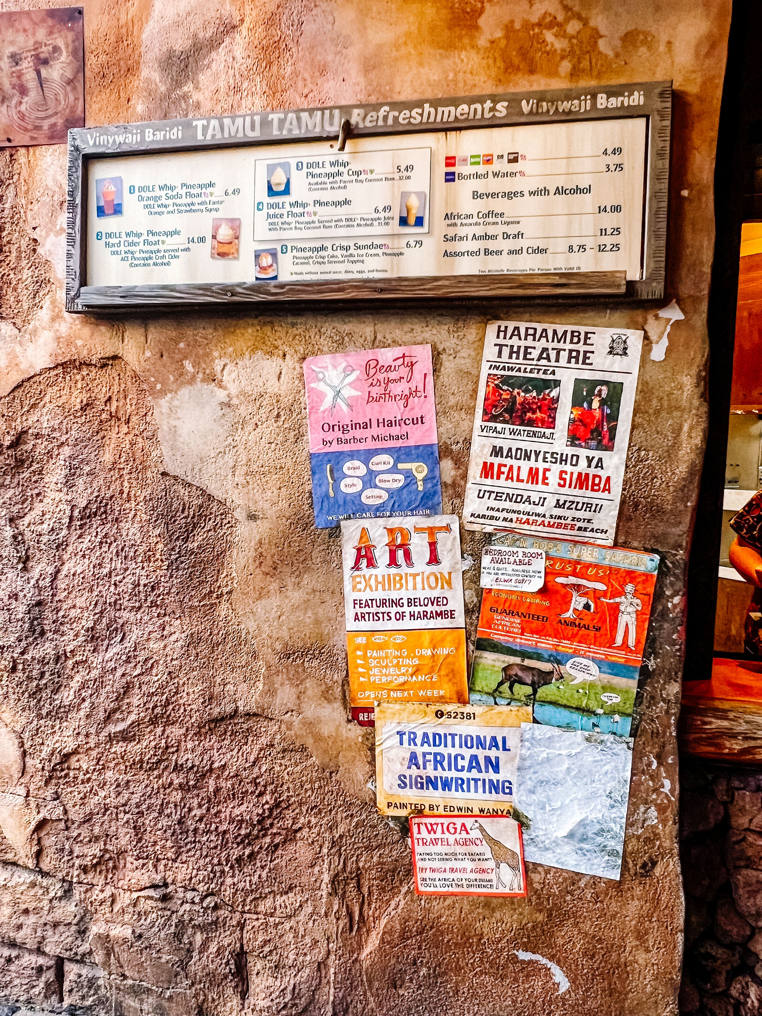 A weathered wall displays a vintage-style menu board and various colorful event posters for local art exhibitions and performances.