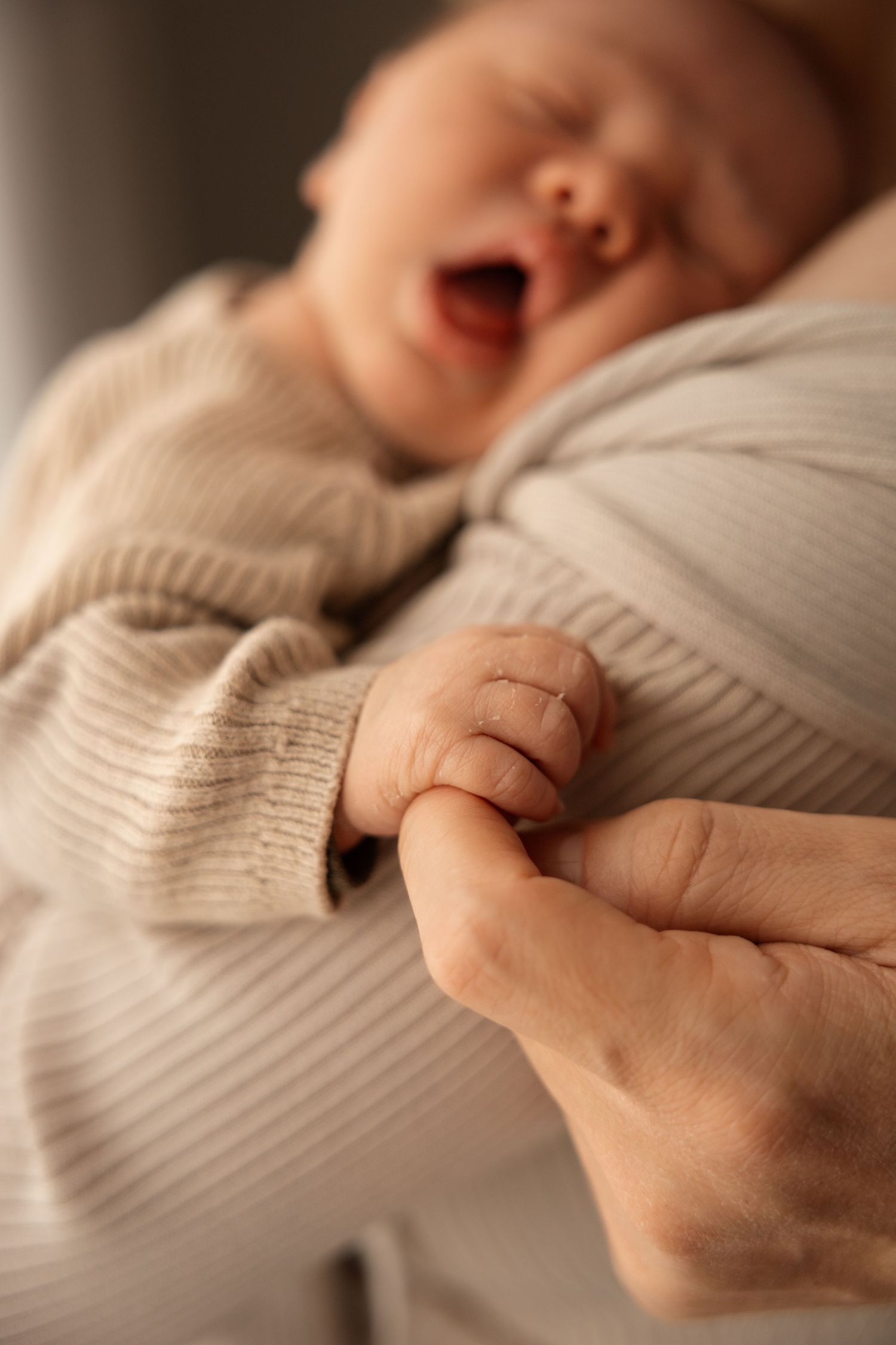 in home newborn session, mum holding baby and dad holding baby hand in christchurch