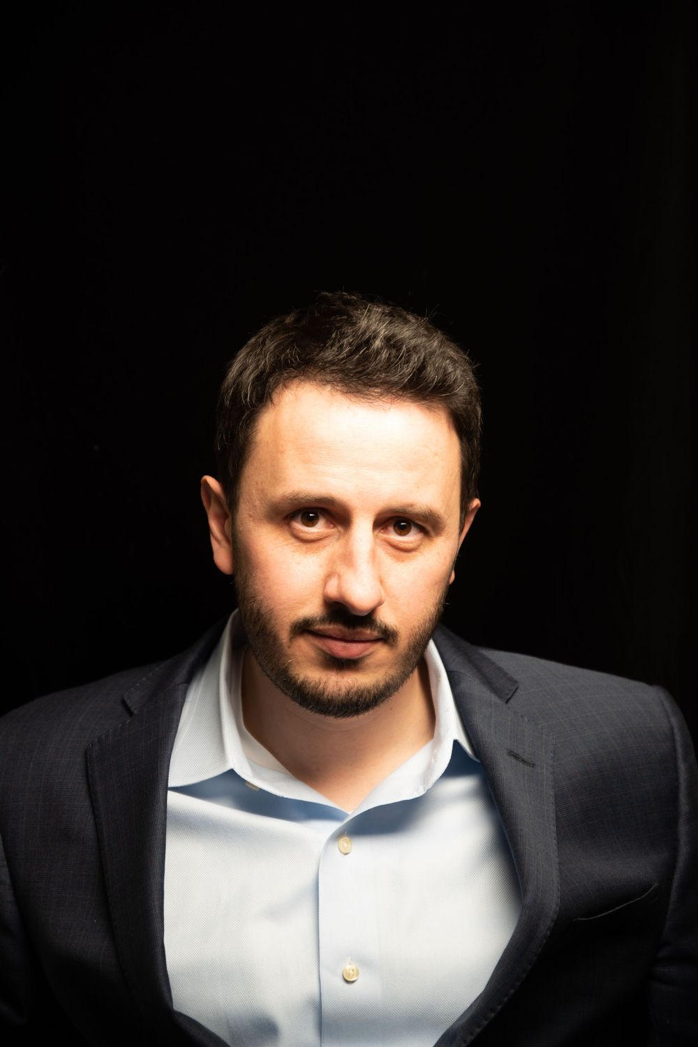 Dramatic portrait of a person in business attire against black background with dramatic lighting.