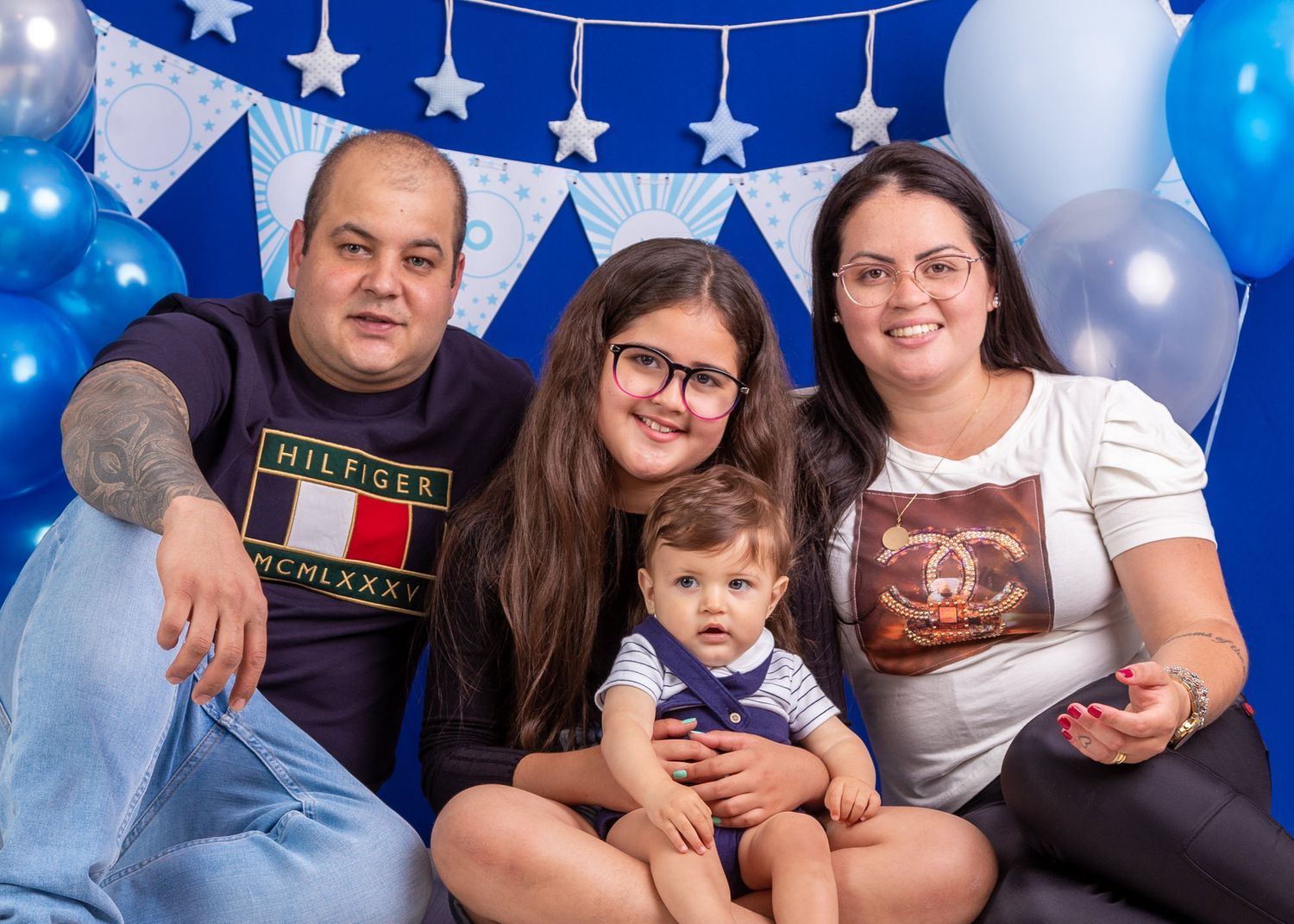 A family poses together for a portrait against a blue and white backdrop with stars and balloons for decoration.