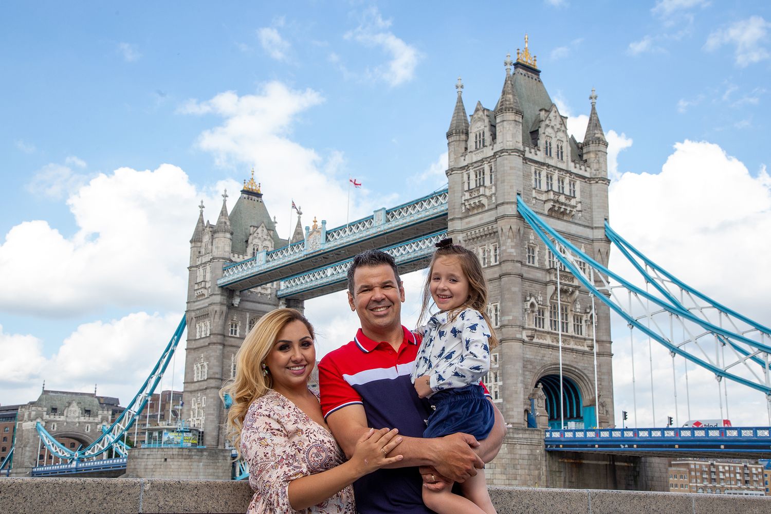 A cheerful family poses together in front of the iconic Tower Bridge in London on a sunny summer day.