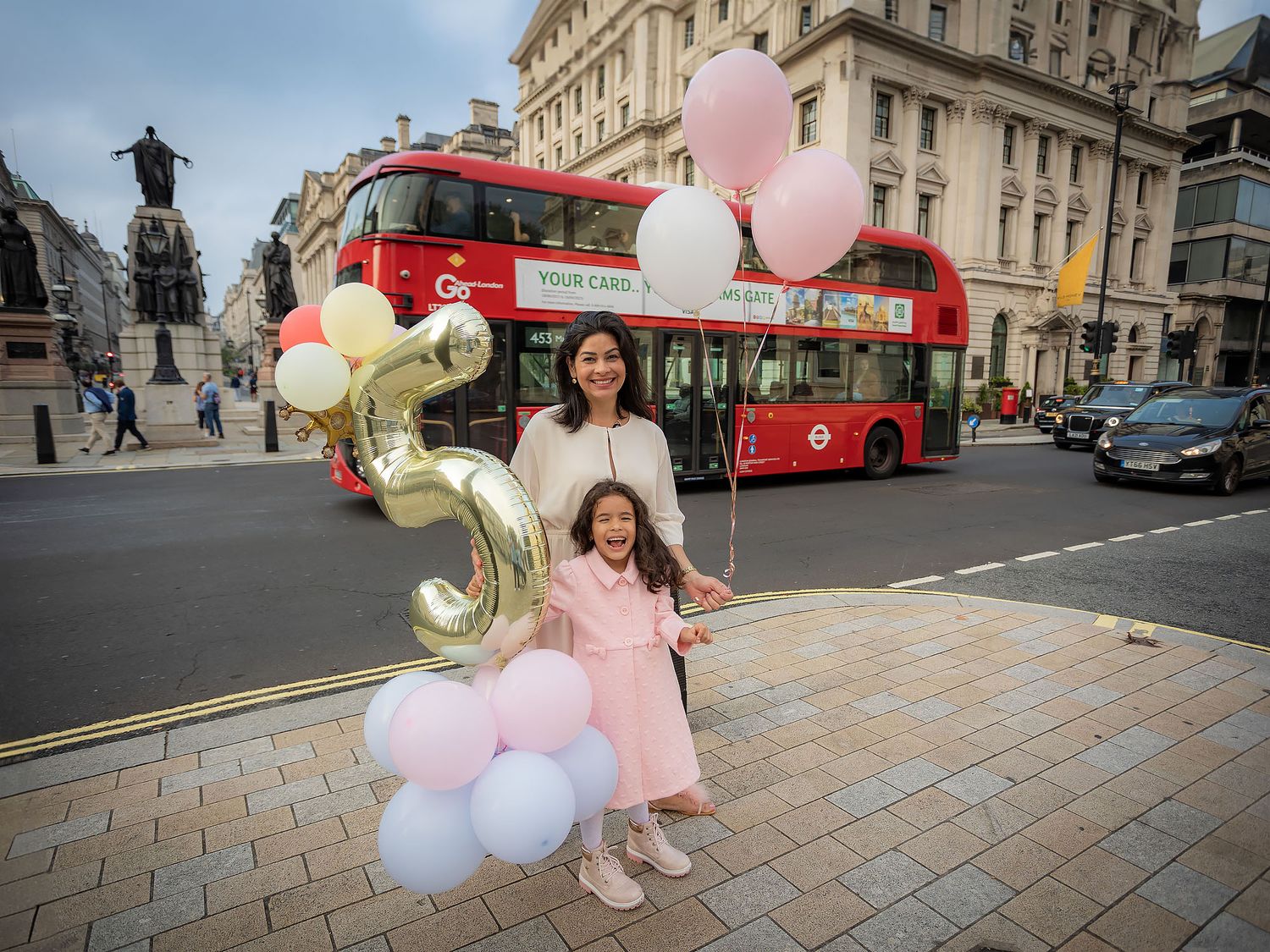 A joyful scene in London with pink and white balloons, a red double-decker bus, and celebration decorations on a city street.