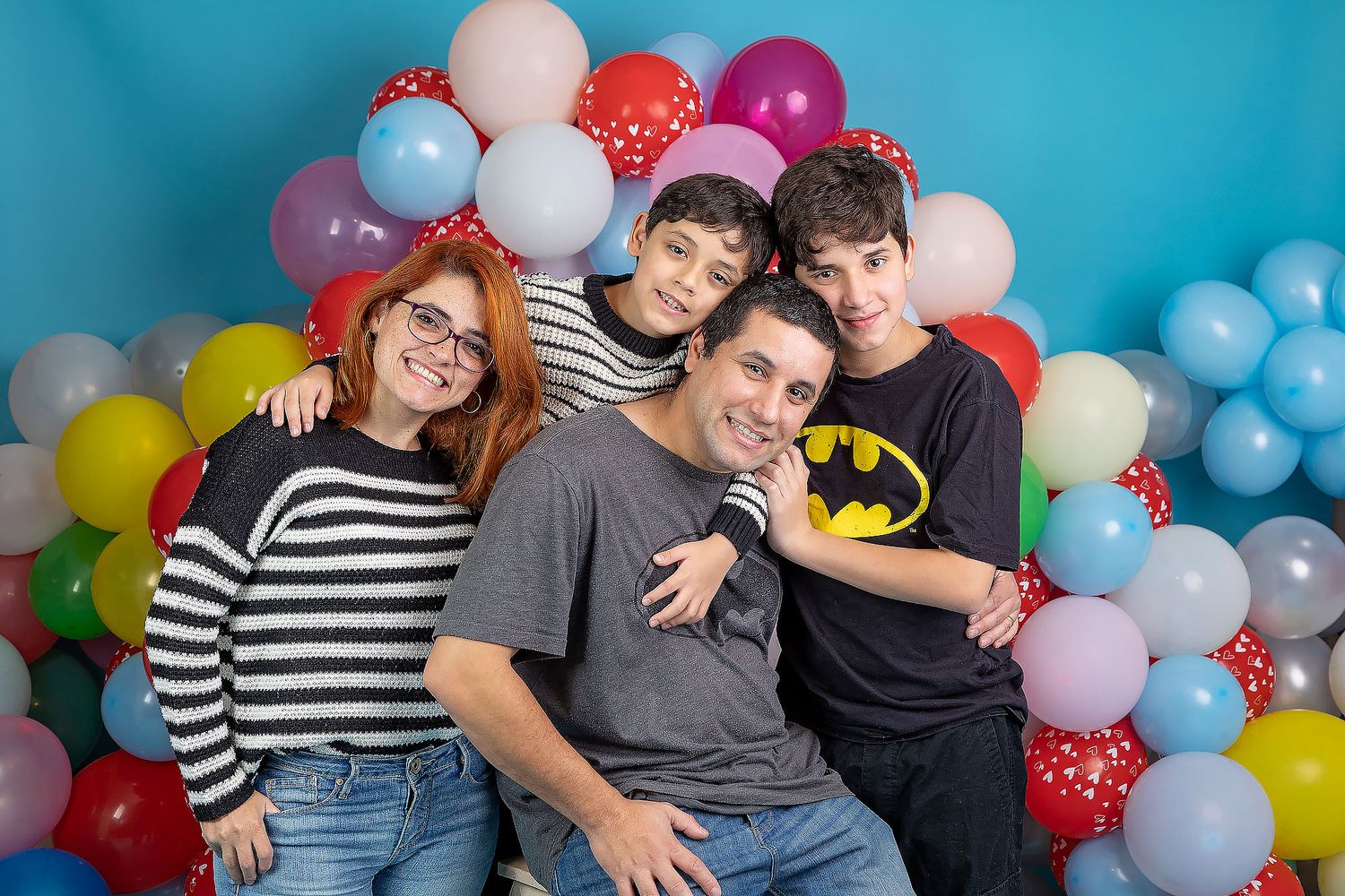 Group posing together against colorful balloon backdrop with pink, blue, white and red balloons at festive celebration.
