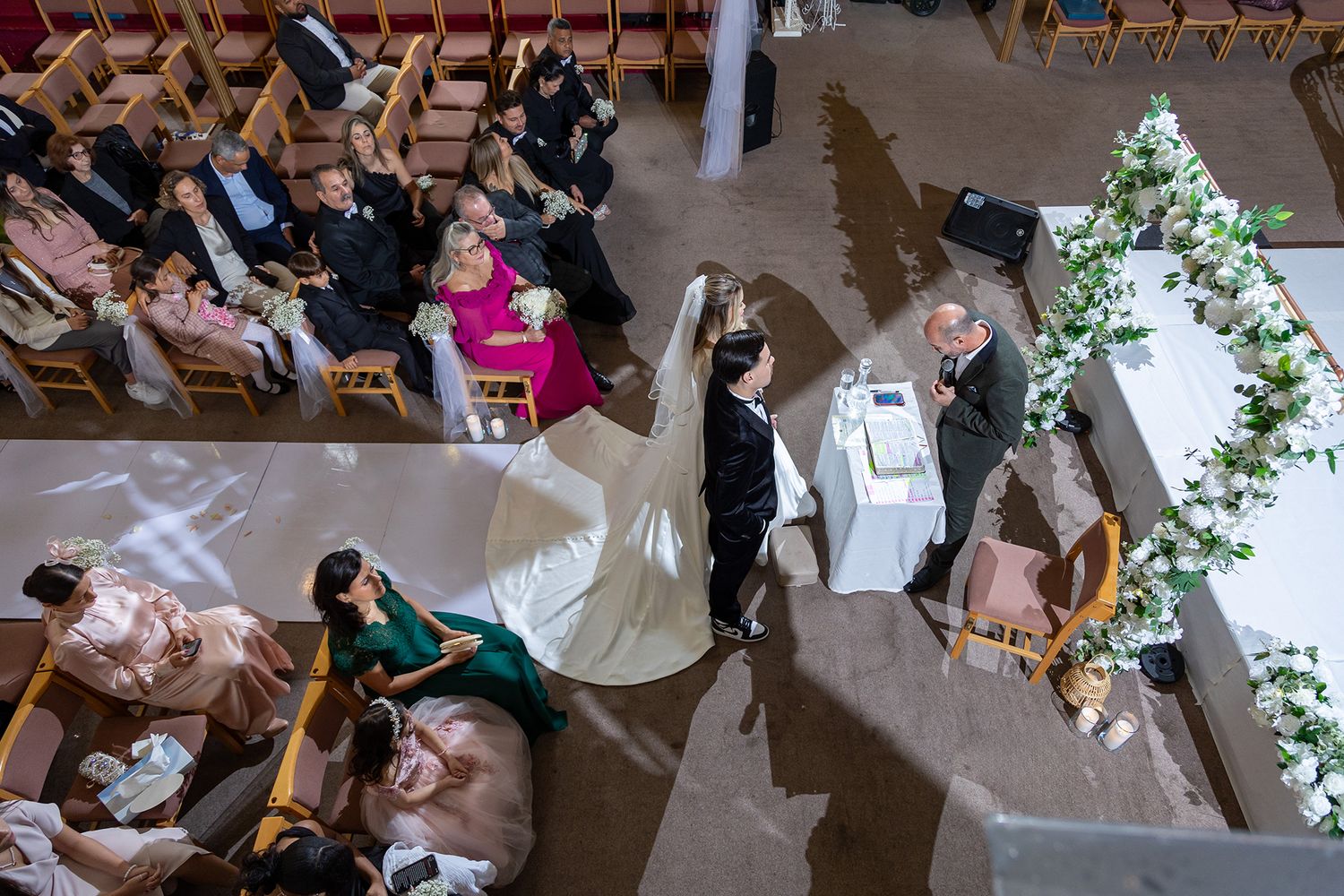 Overhead view of a wedding ceremony featuring guests and a couple exchanging vows in a church with floral decorations.