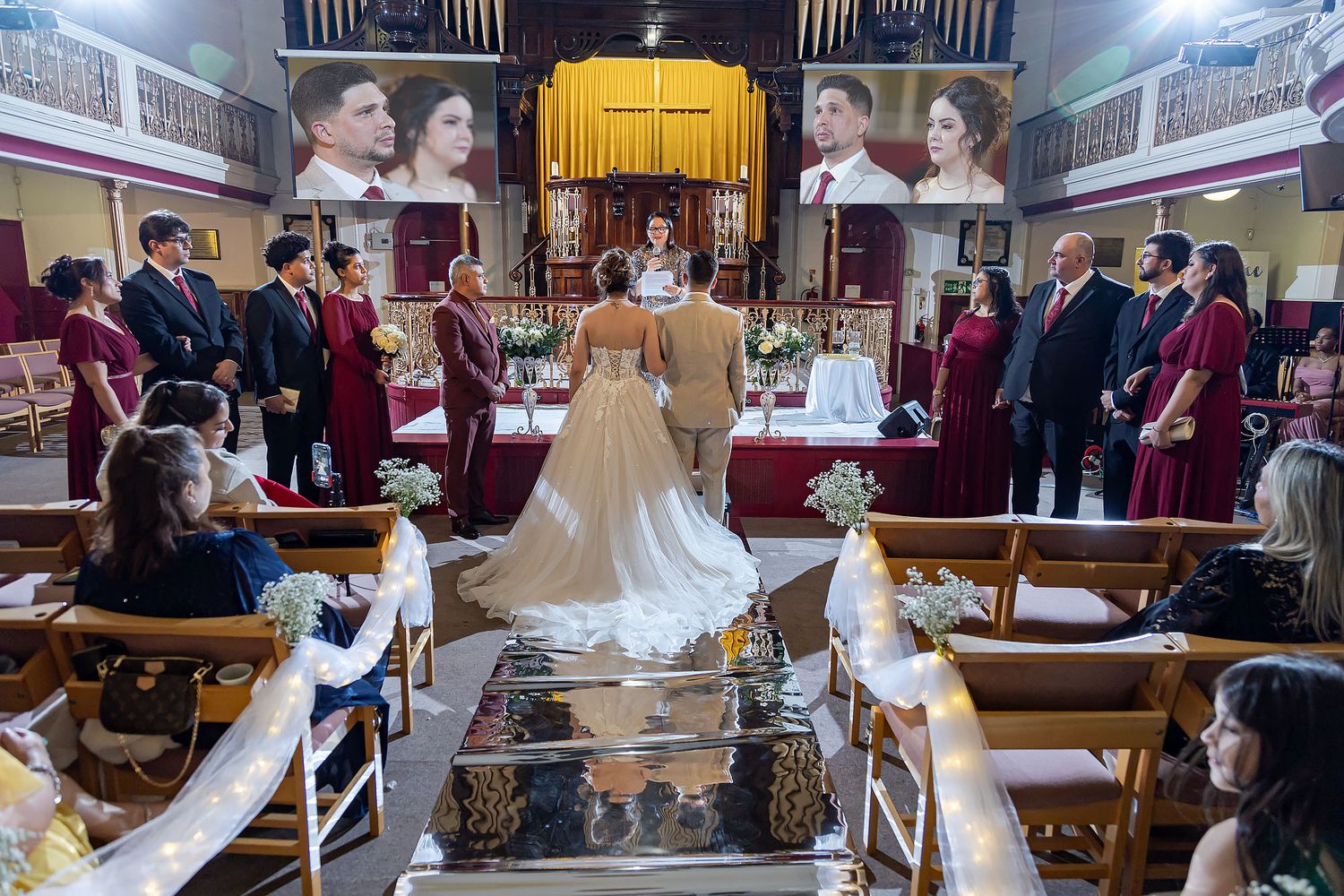 A wedding ceremony taking place in a historic church with wooden pews and balcony seating, captured from behind the congregation.