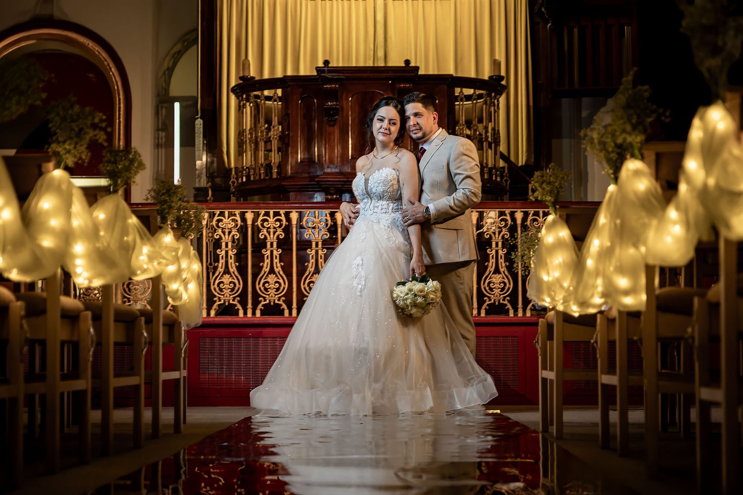 Beautiful wedding ceremony in a church sanctuary with glowing candles lining the aisle and ornate altar railing.