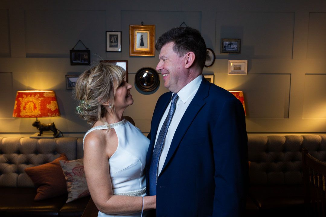 A couple shares a tender moment together in a dimly lit room with vintage decor and lamps.