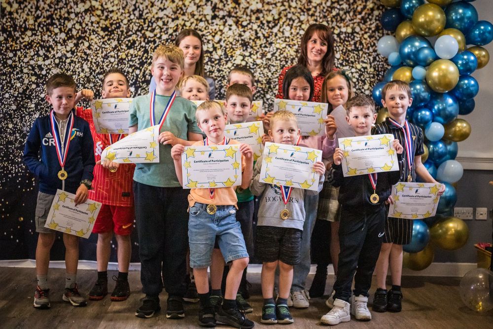 Group of happy junior hockey players holding up certificates to the camera in front of a backdrop and balloon arch with their coach