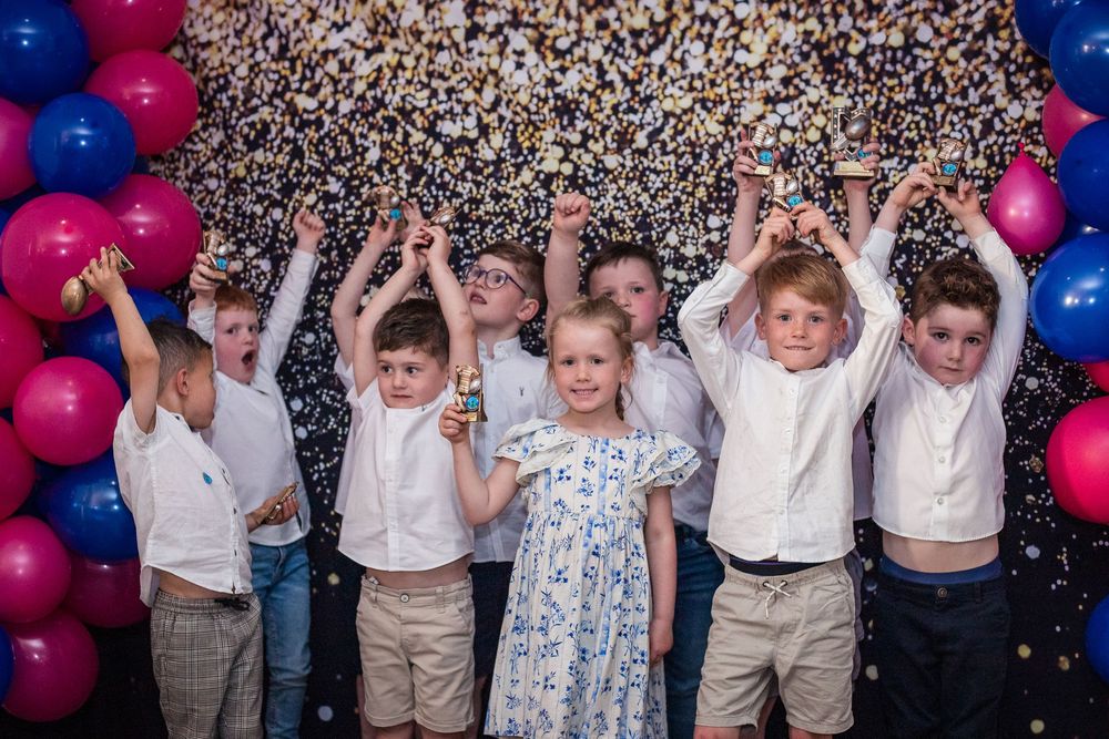 Group of young rugby players wearing white shirts looking at a screen with happy faces at Junior Awards Night with balloon garland.