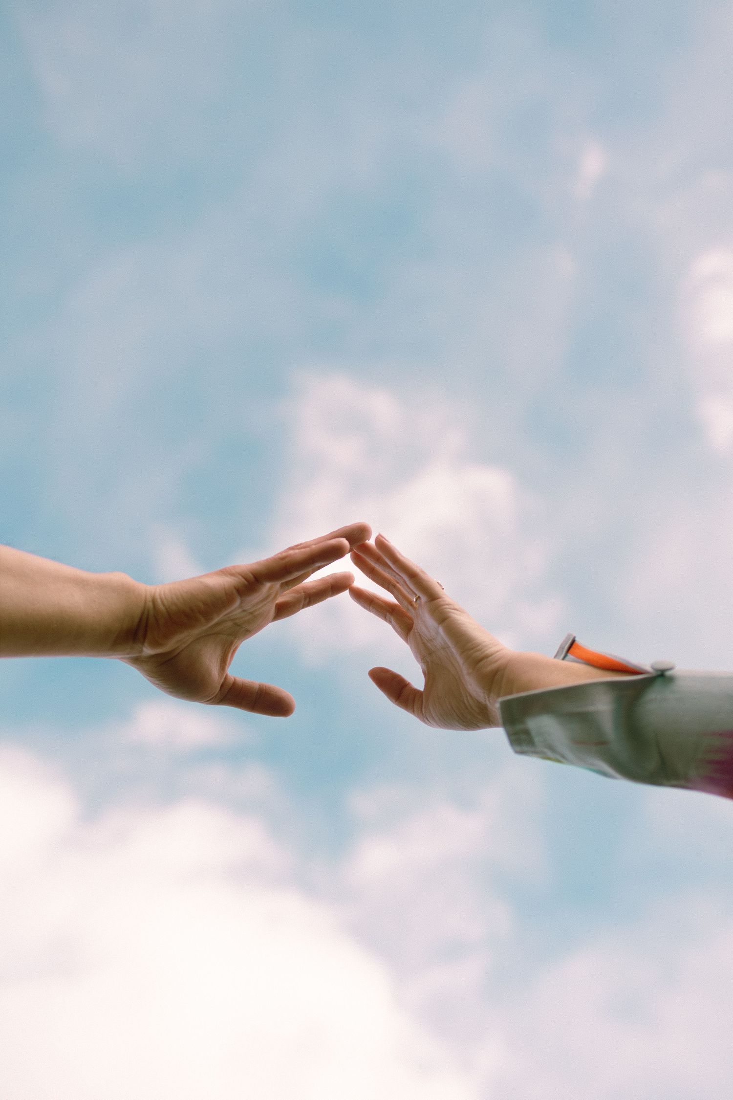 Two hands reaching toward each other against a blue sky, reminiscent of Michelangelo's Creation of Adam.