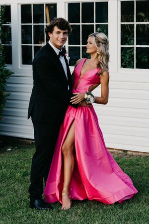 Formal couple poses by white house, with woman in striking pink gown with thigh-high slit.