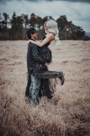 Romantic couple embracing in sepia-toned field with moody sky backdrop.
