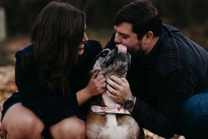 A couple shares a tender moment with their fluffy dog in a warm autumn setting.