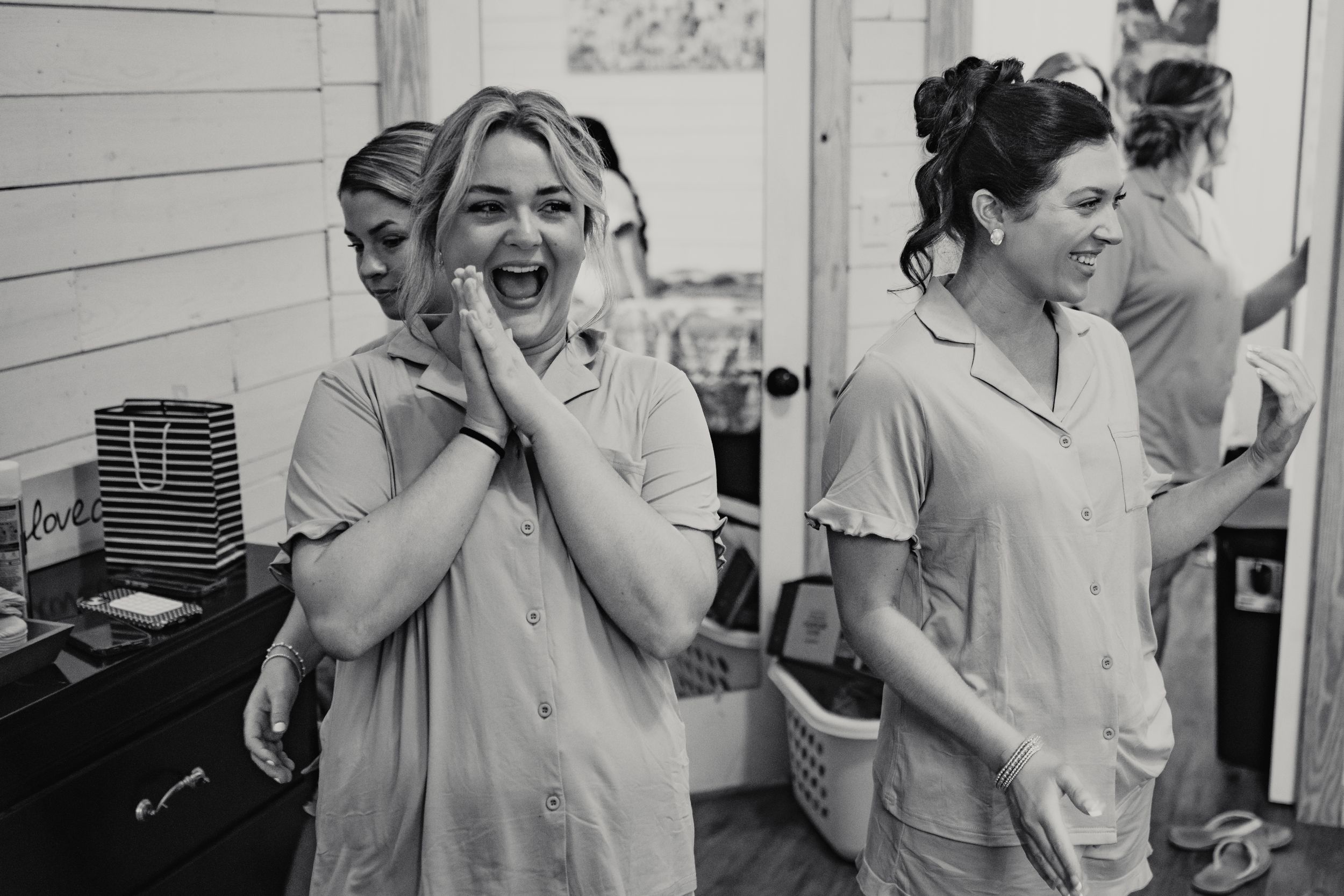 Black and white photo of bridesmaids in matching pajamas laughing joyfully while getting ready for a wedding.