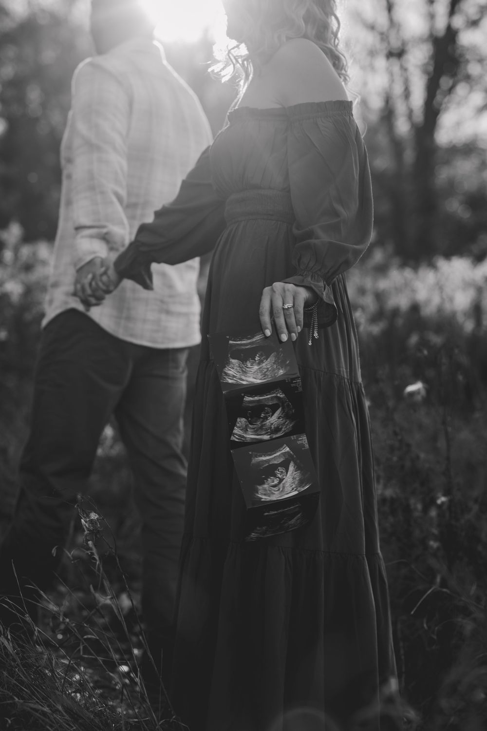 A monochrome image showing an ultrasound scan being held against a long black dress in natural sunlight.