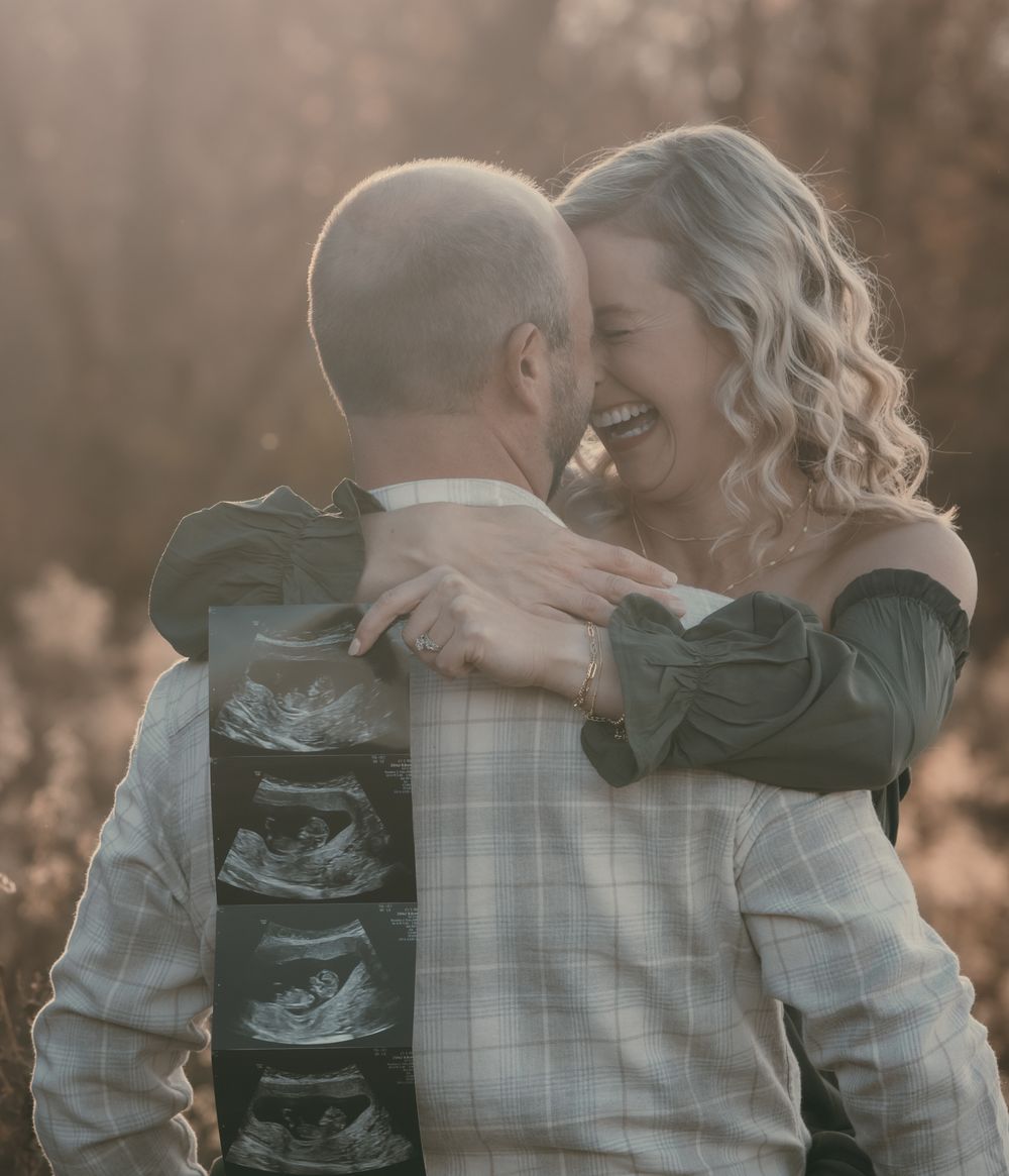 A romantic outdoor portrait of an expecting couple embracing and laughing while holding ultrasound photos.
