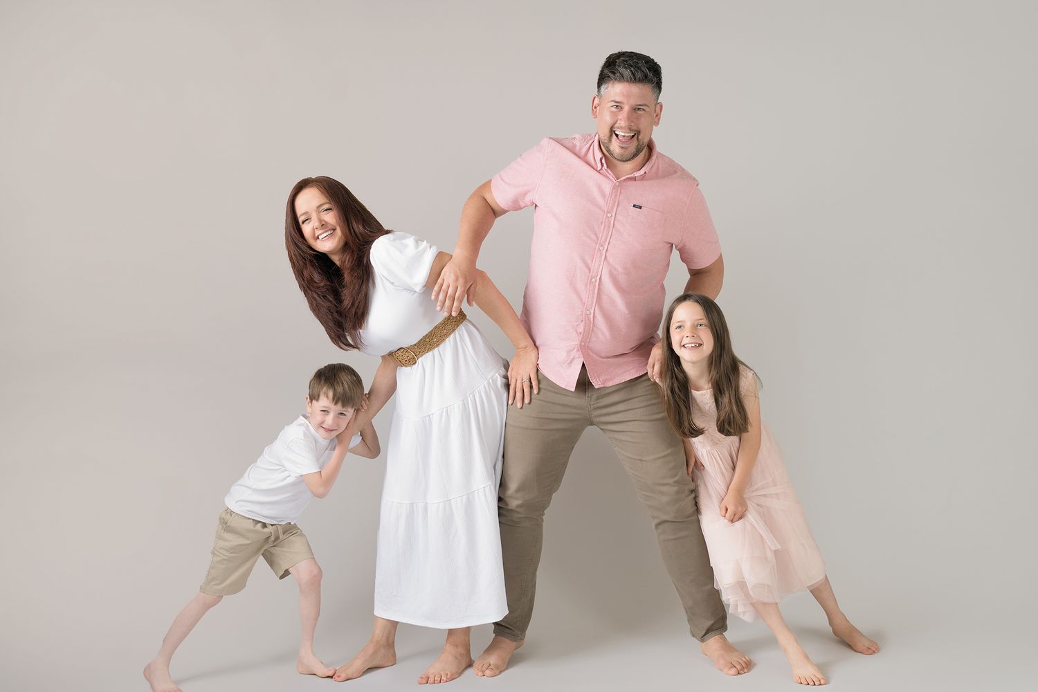 Four people in matching pink and neutral outfits pose playfully against a light gray studio backdrop.