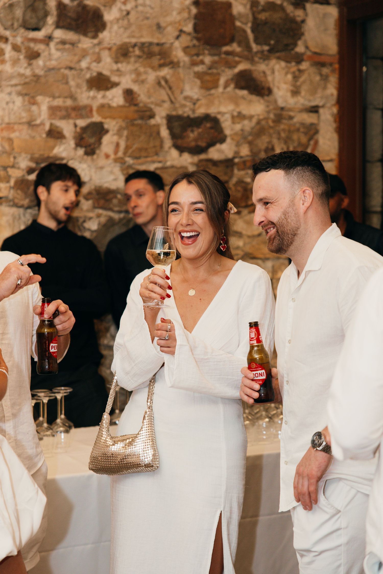 Wedding guests enjoy drinks and laughter at a rustic stone venue reception.