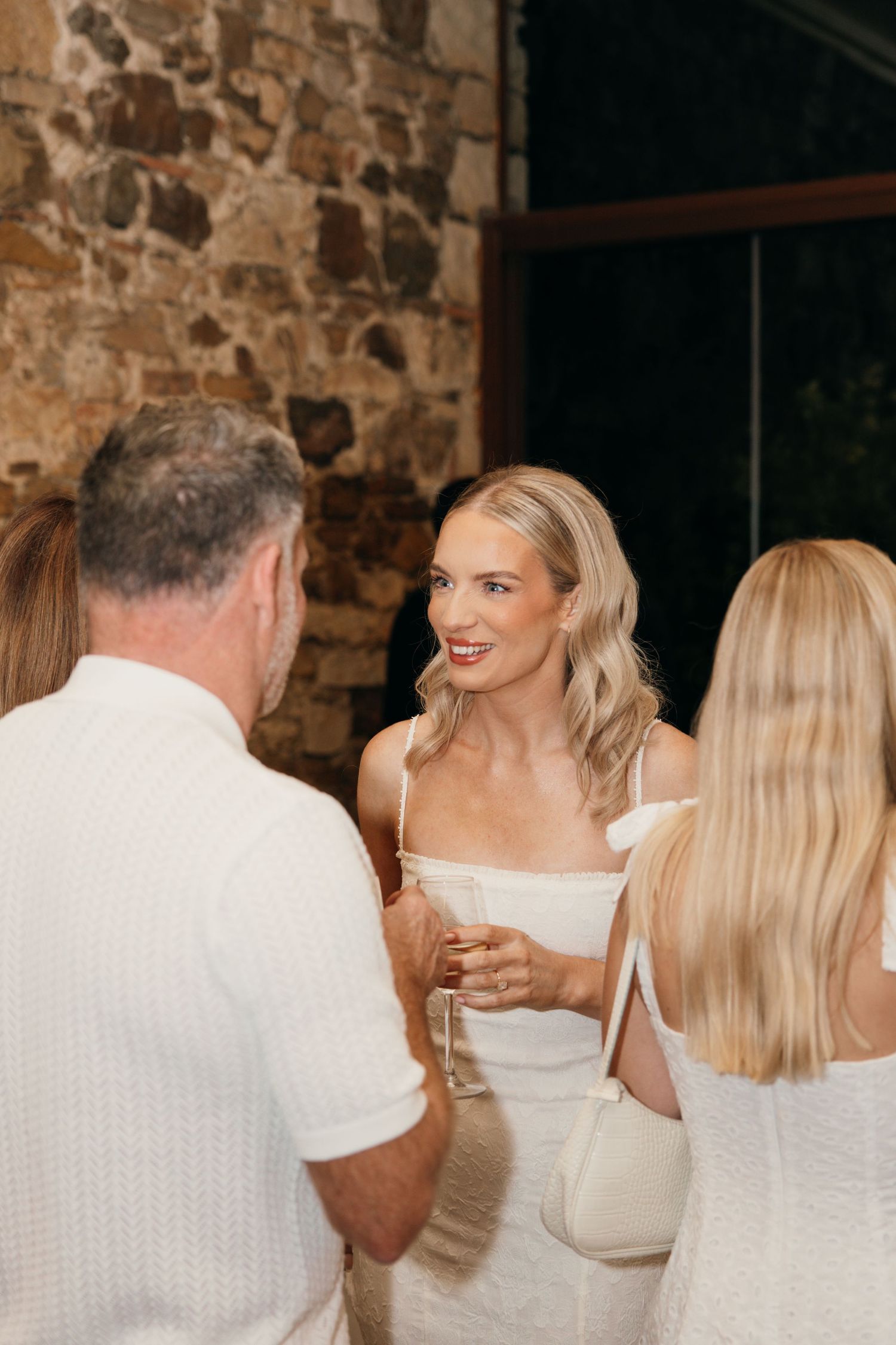 Elegant party guests mingling and conversing in front of stone walls at an upscale event.