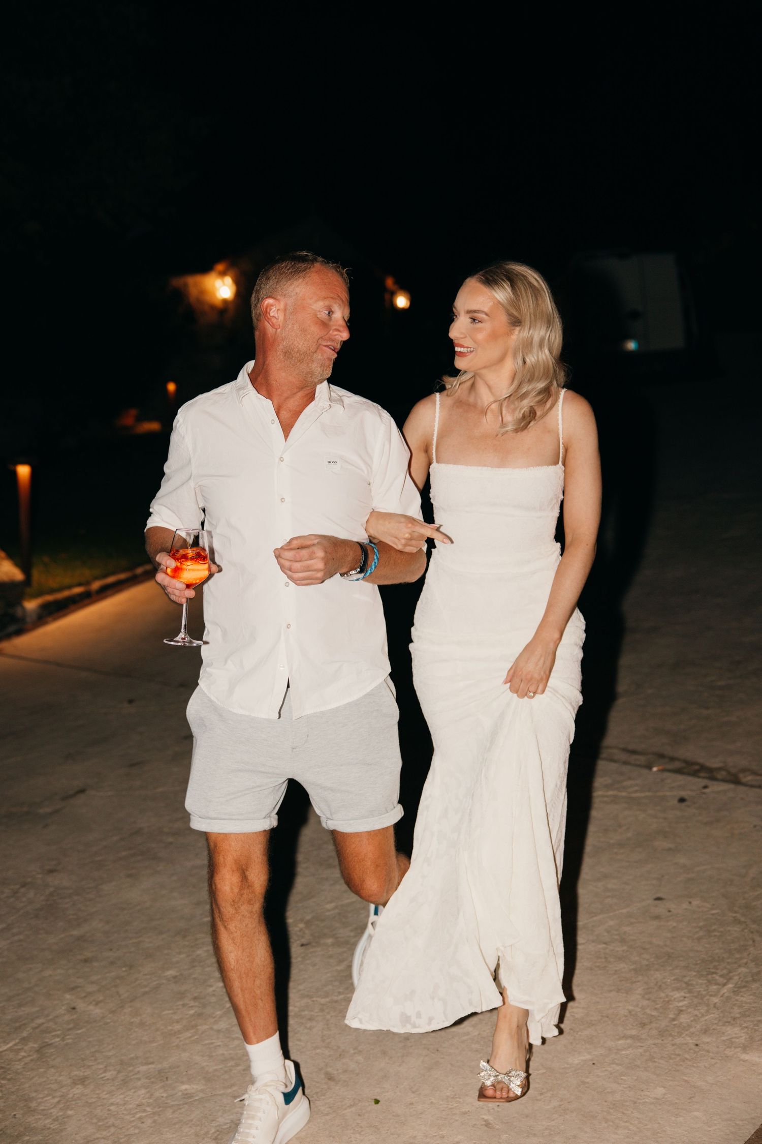 Evening celebration with guests in white attire walking along a lit pathway.