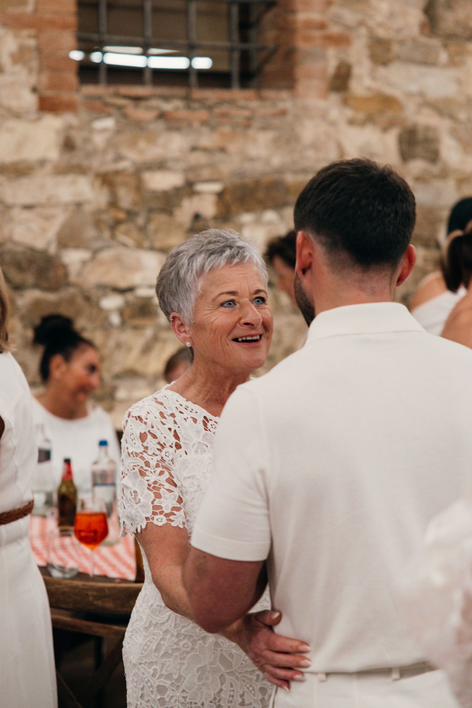 A candid moment of guests enjoying conversation at a wedding reception in a rustic stone venue.