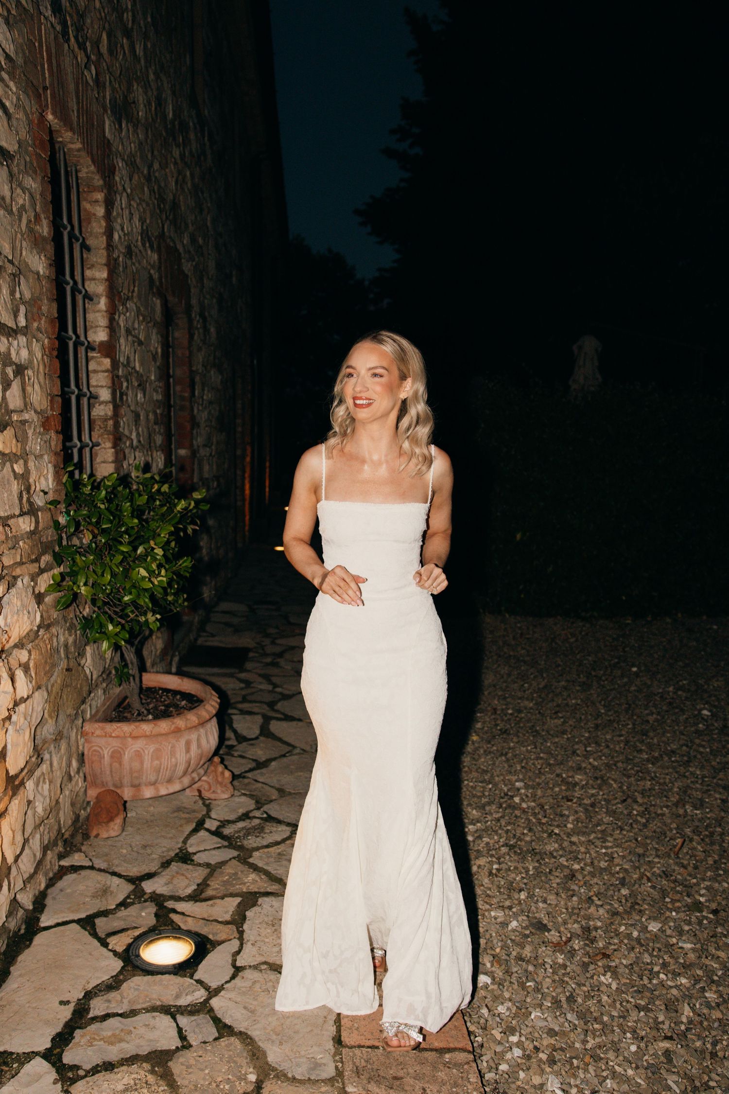 A radiant bride laughs while posing in her fitted white gown on a stone pathway.