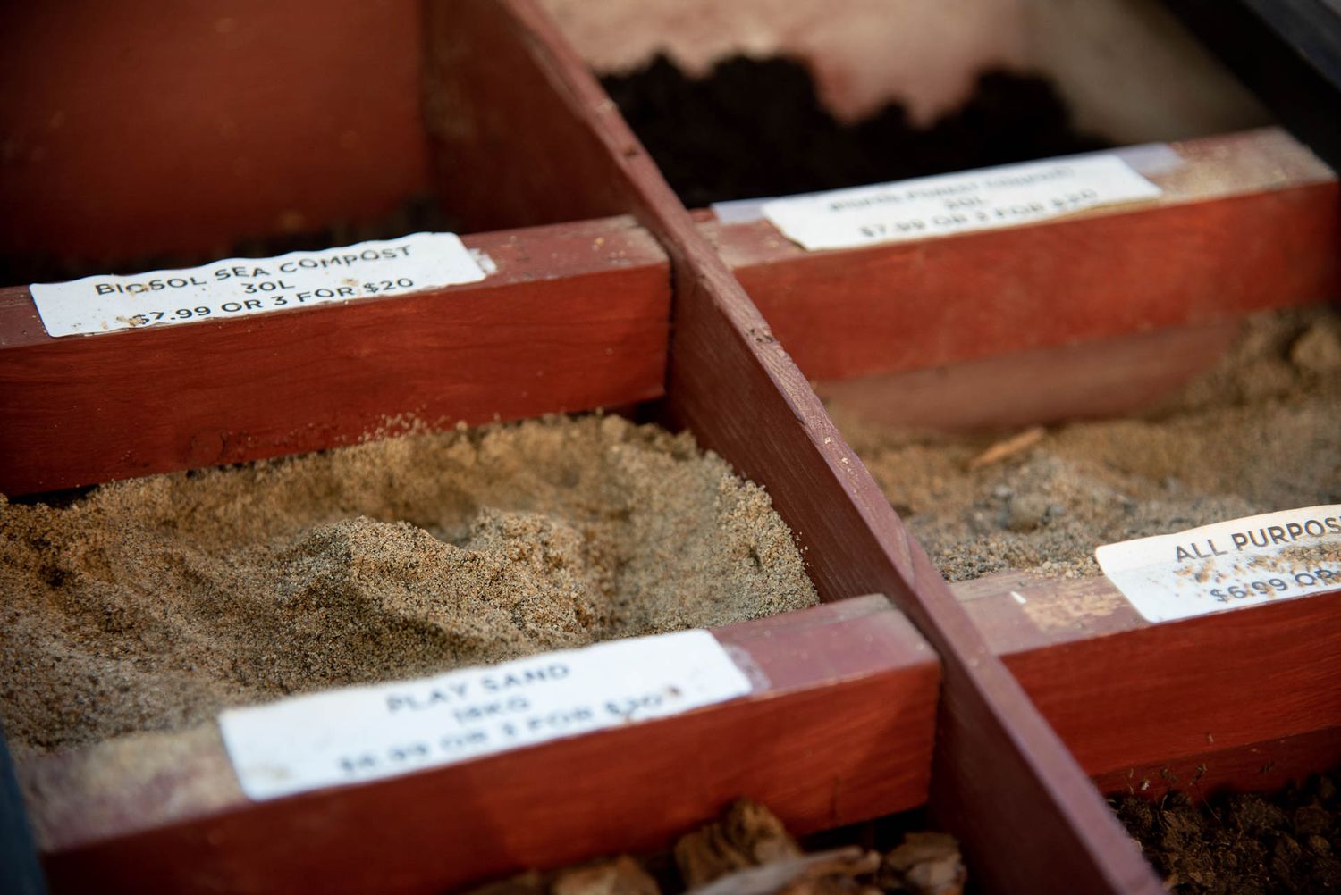 Red wooden seed planting trays filled with soil and labeled tabs showing organized gardening plots at Bradford Greenhouse in Barrie, ON
