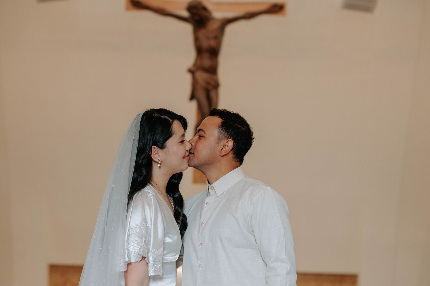 A couple sharing a tender moment in a church with a crucifix mounted on the wall behind them.