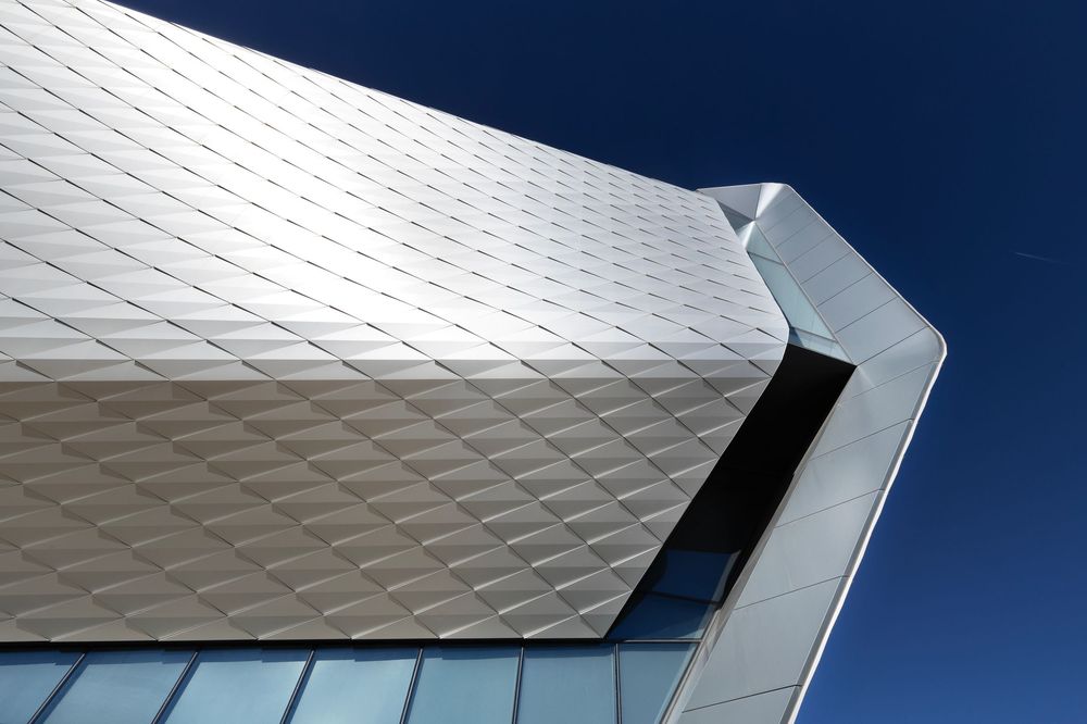 Olympic and Paralympic Museum abstract pattern of white geometric panels on modern building facade against deep blue sky.