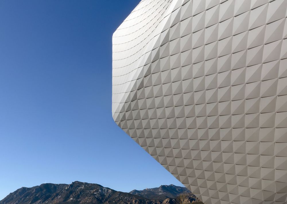 Olympic and Paralympic Museum textured white geometric facade of modern building with mountains in background.