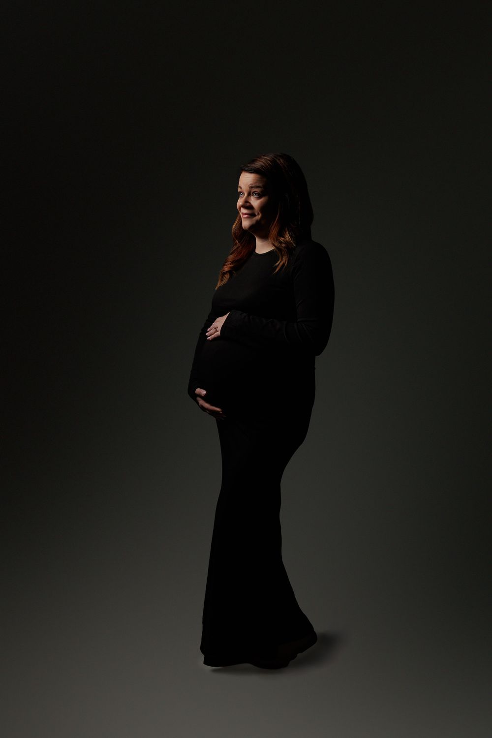 A series of moody black and white maternity portraits showing a pregnant woman in a dark dress against a shadowy background.