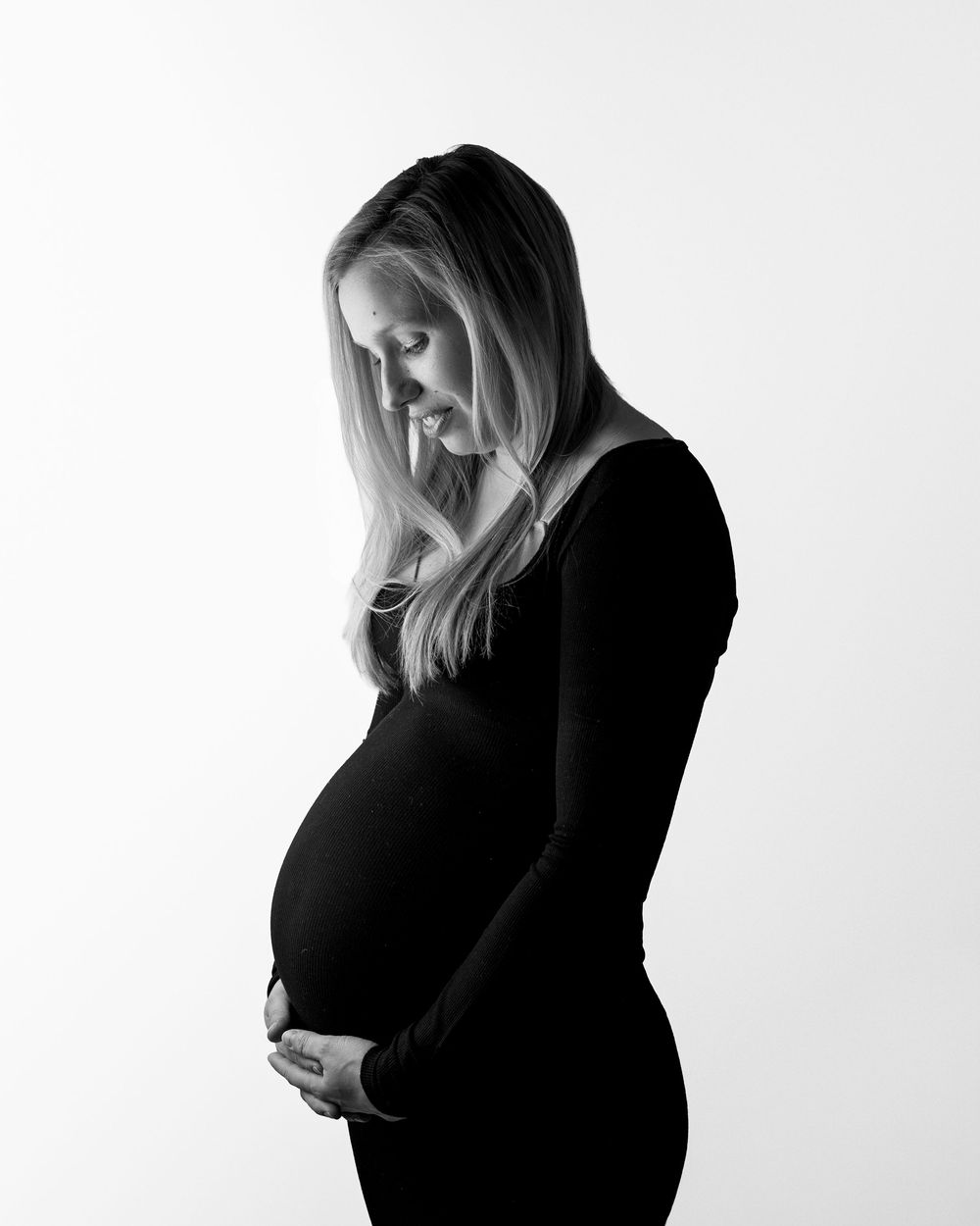 Black and white artistic maternity portrait showing silhouette of an expectant mother in a dark dress against light background.