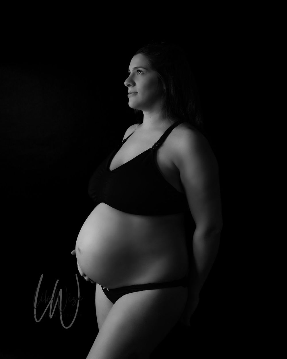 A dramatic black and white artistic maternity photo showing an intimate silhouette against a dark background.
