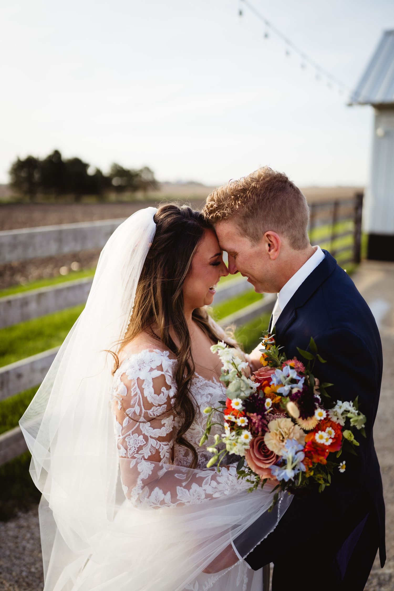 A sweet tender moment between newlyweds outdoors with a beautiful colorful bouquet and lace wedding dress details.