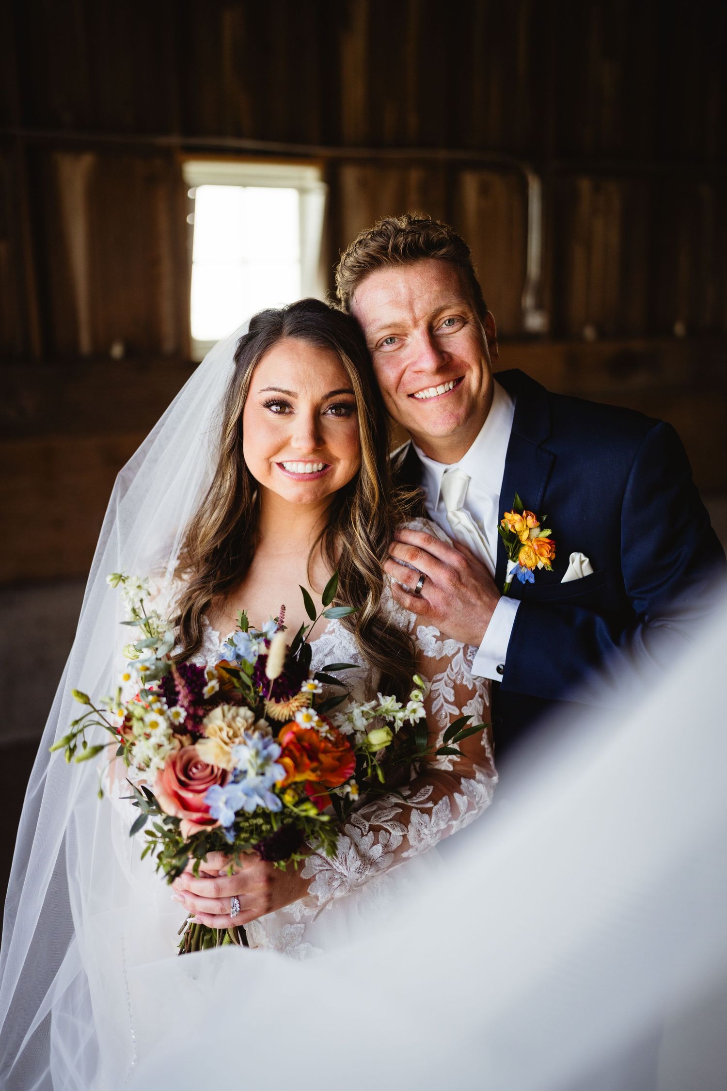A wedding portrait featuring a couple in formal attire with a colorful bouquet inside a rustic wooden venue.