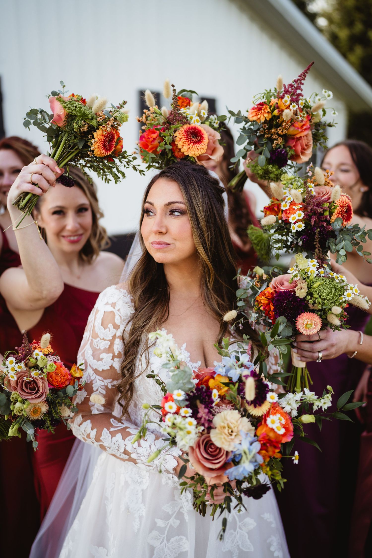 Beautiful wedding bouquets with coral and peach roses, held by group in burgundy dresses and white lace gown.