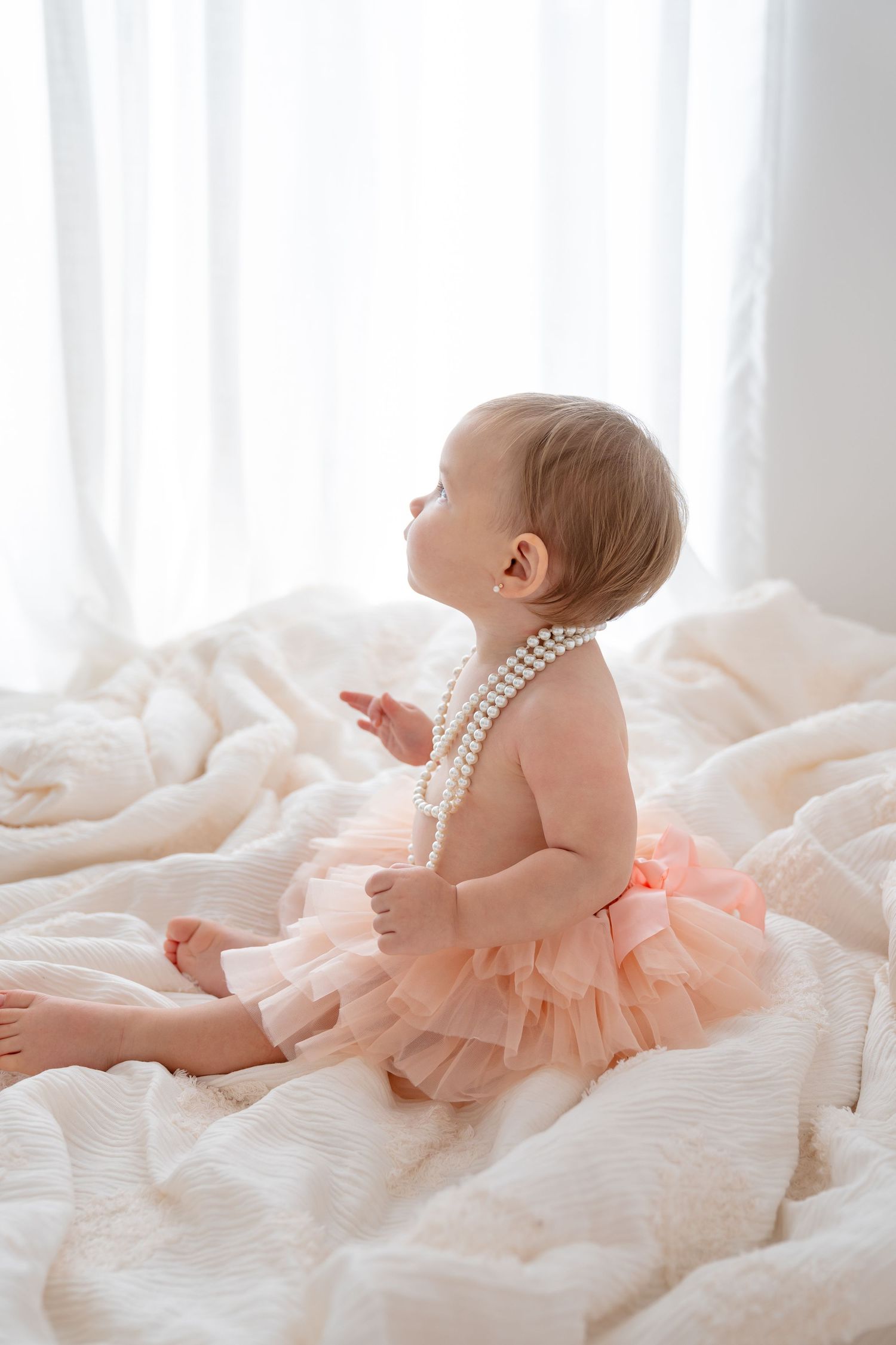 A newborn baby being gently held in white sleeves against a light-filled window with a soft yellow blanket.