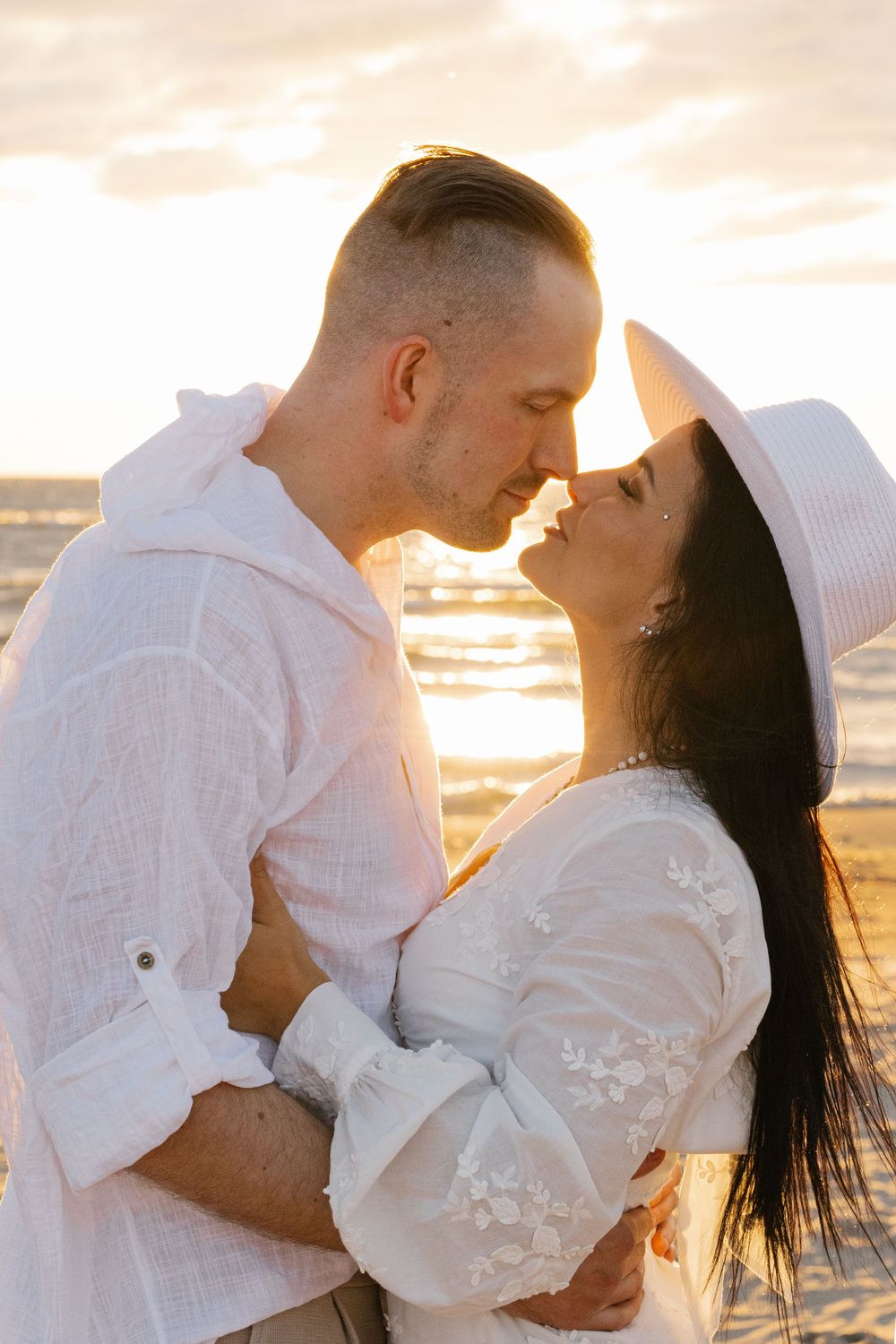 A couple shares an intimate moment at sunset on the beach, with golden light glowing behind them.