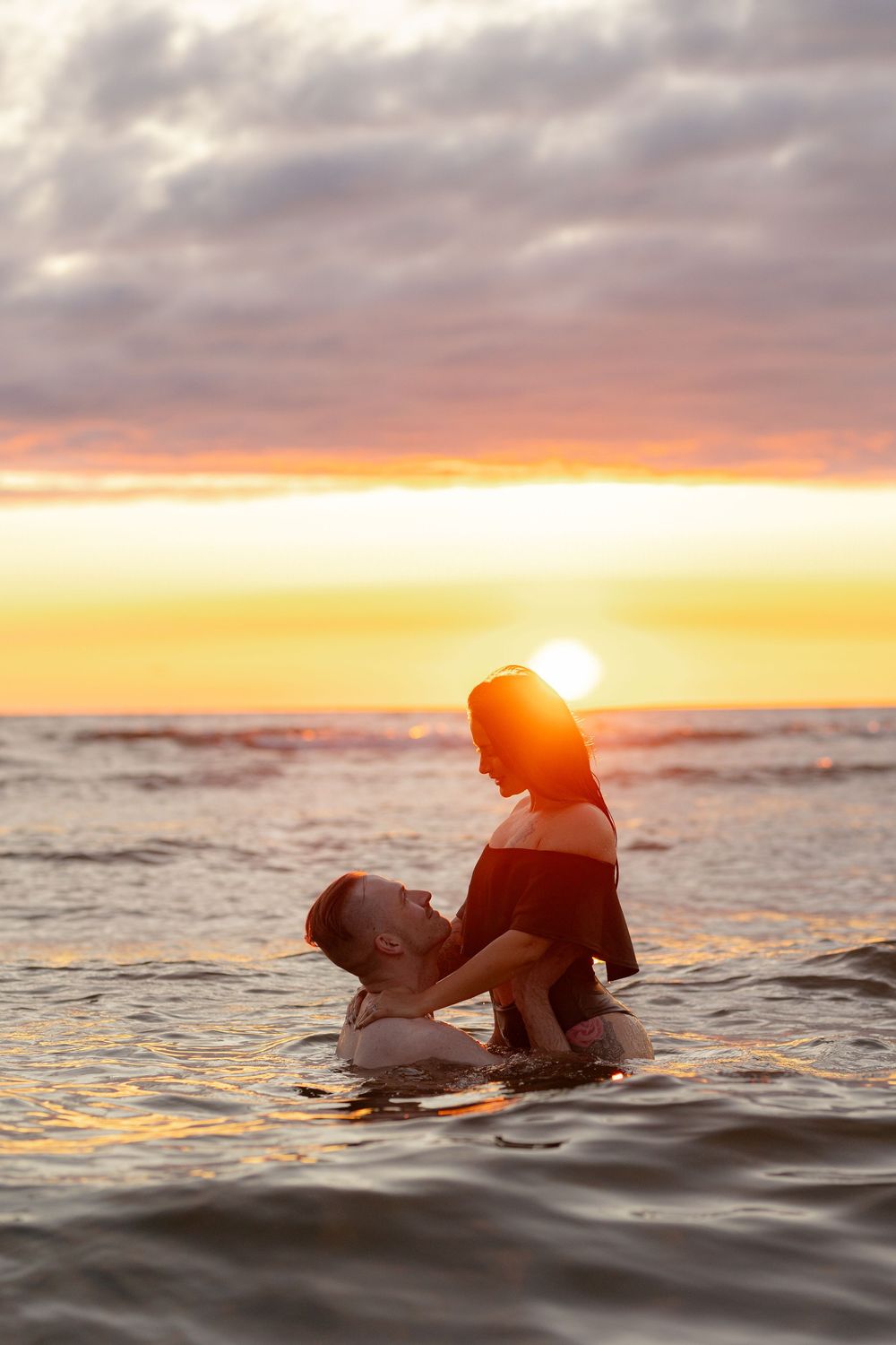 Two people enjoying a romantic moment in the ocean water during a vibrant golden sunset.