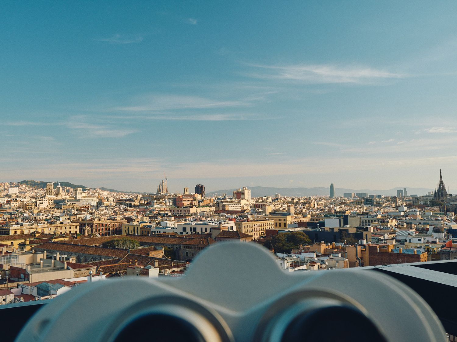 Tourist viewpoint through coin operated binoculars overlooking rooftops and skyline of Barcelona on sunny day.