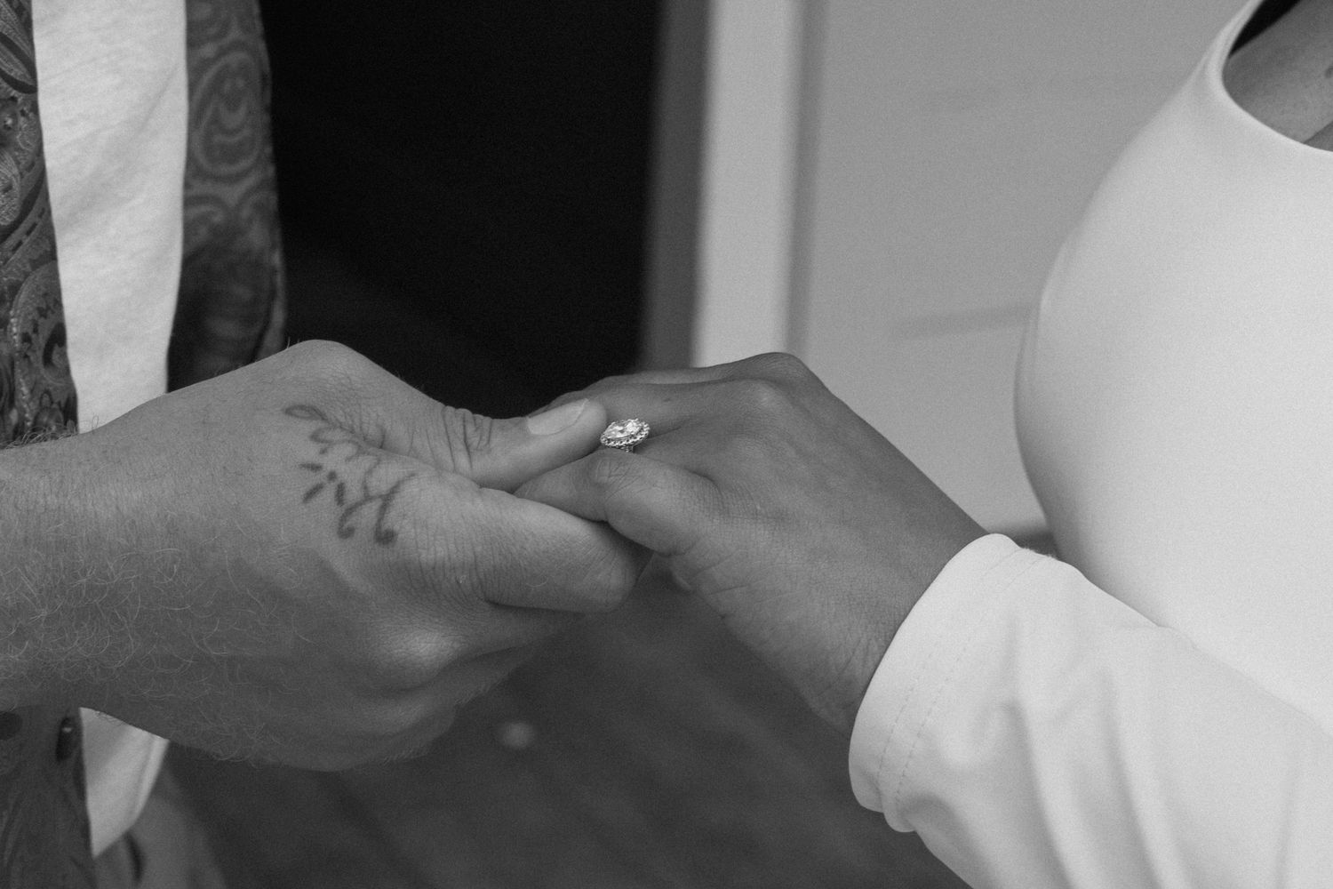 Black and white photo showing two hands exchanging a ring during a wedding ceremony.