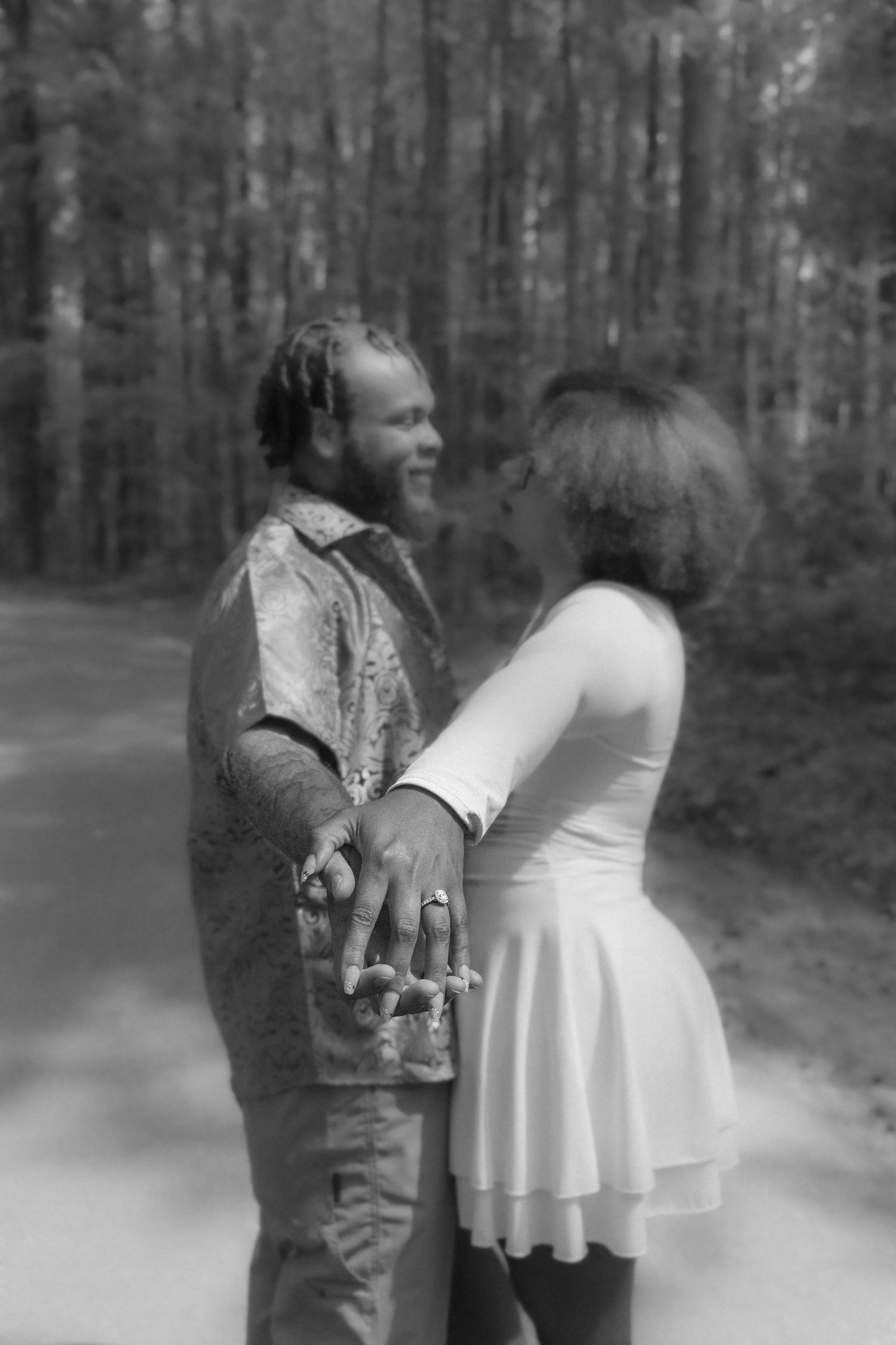 A dreamy black and white photograph of a couple embracing on a misty forest path.