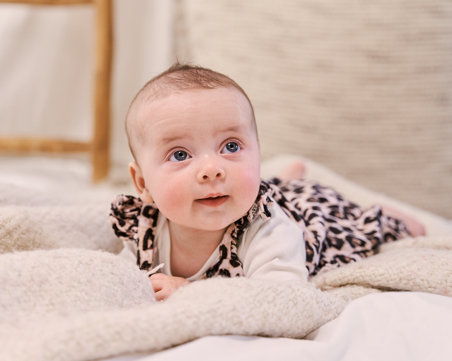 Baby in leopard print outfit lying on blanket with curious expression.