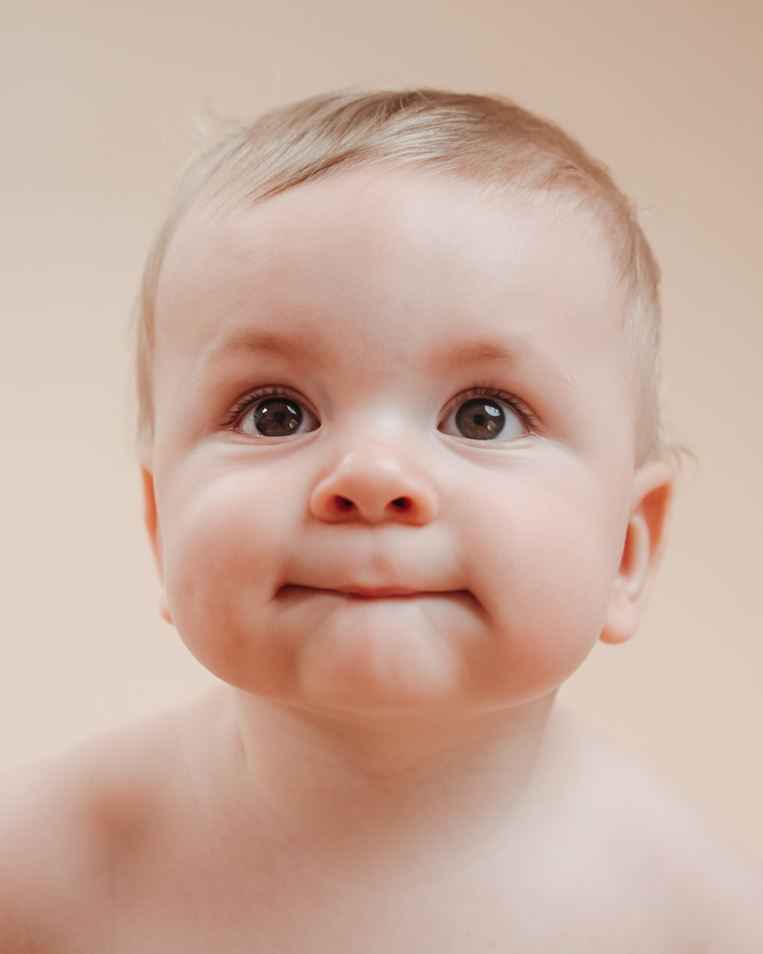 Baby with bright eyes and cheerful expression against neutral background.