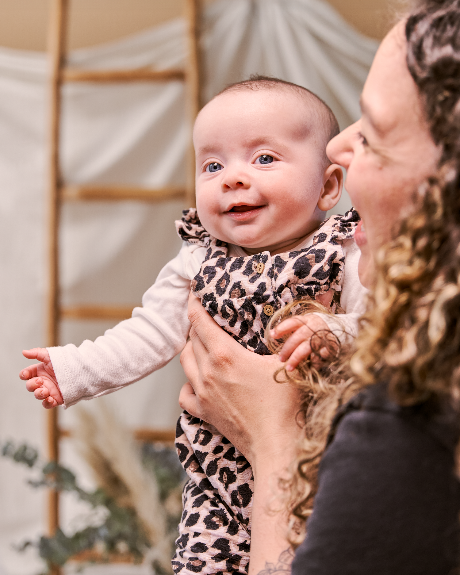 Baby in leopard print outfit smiles joyfully while being held up in the air.
