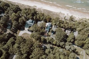 Aerial view of beachfront homes nestled among dense trees along a sandy coastline with turquoise water.